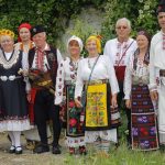 A group of adults and children in traditional Slavic clothing posing outdoors.